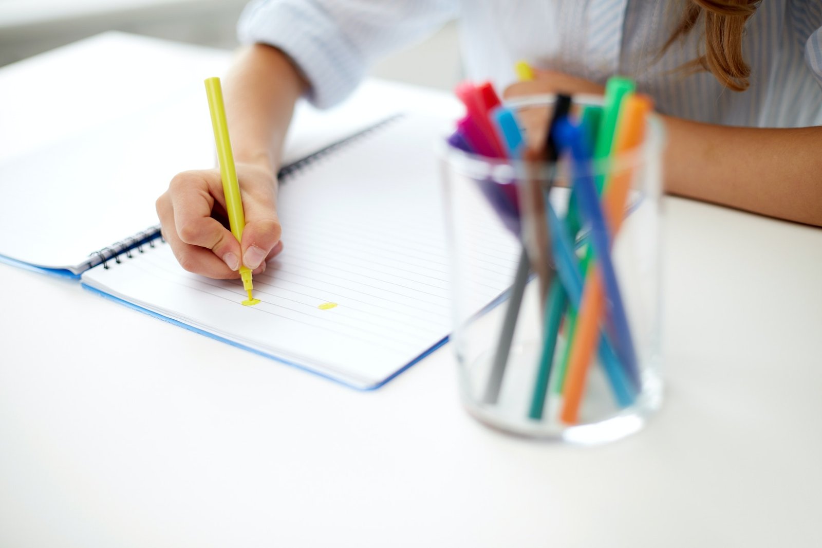 A student writing in a notebook beside colored pencils
