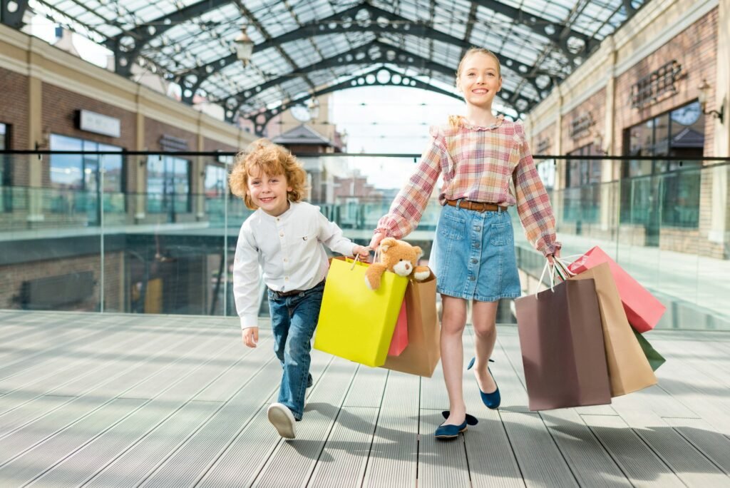 Adorable smiling children holding paper bags together while walking in shopping mall