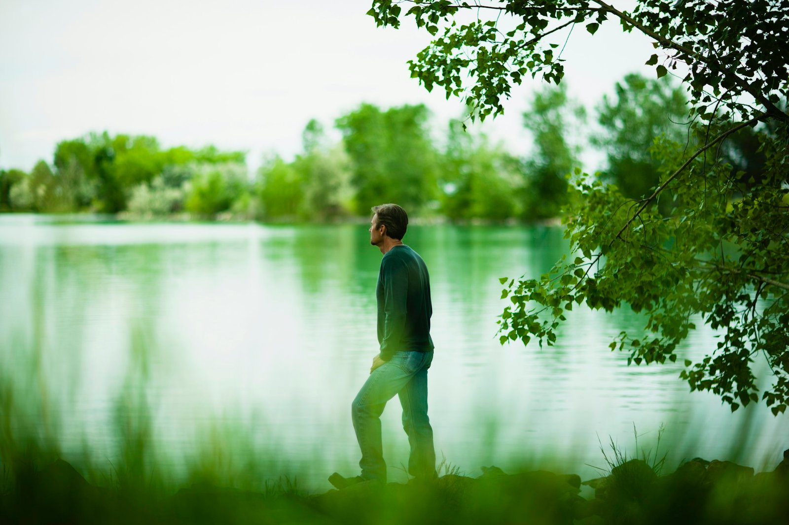 A man standing alone looking into the distance across the water, deep in thought.