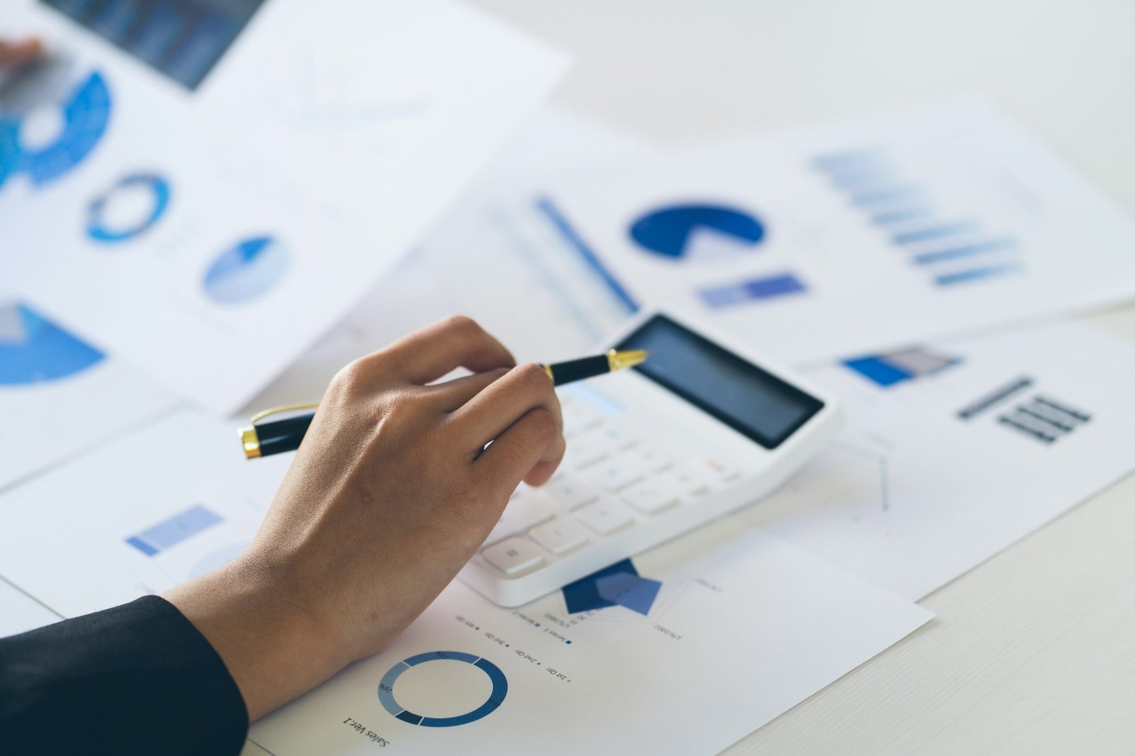 attractive business woman working on table with laptop and caculator and holding pen point on graph