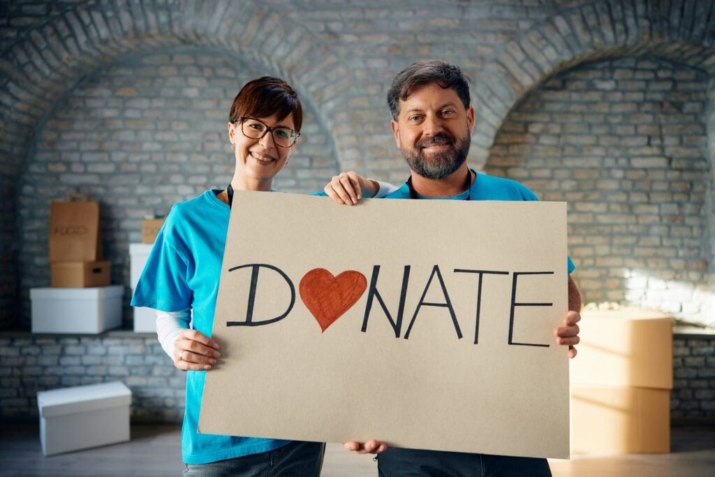 Happy volunteers holding placard with 'donate' message and looking at camera.