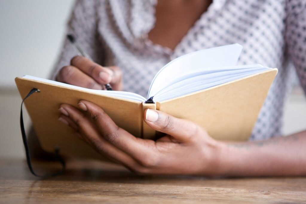 Partial portrait of black female author at home writing in journal