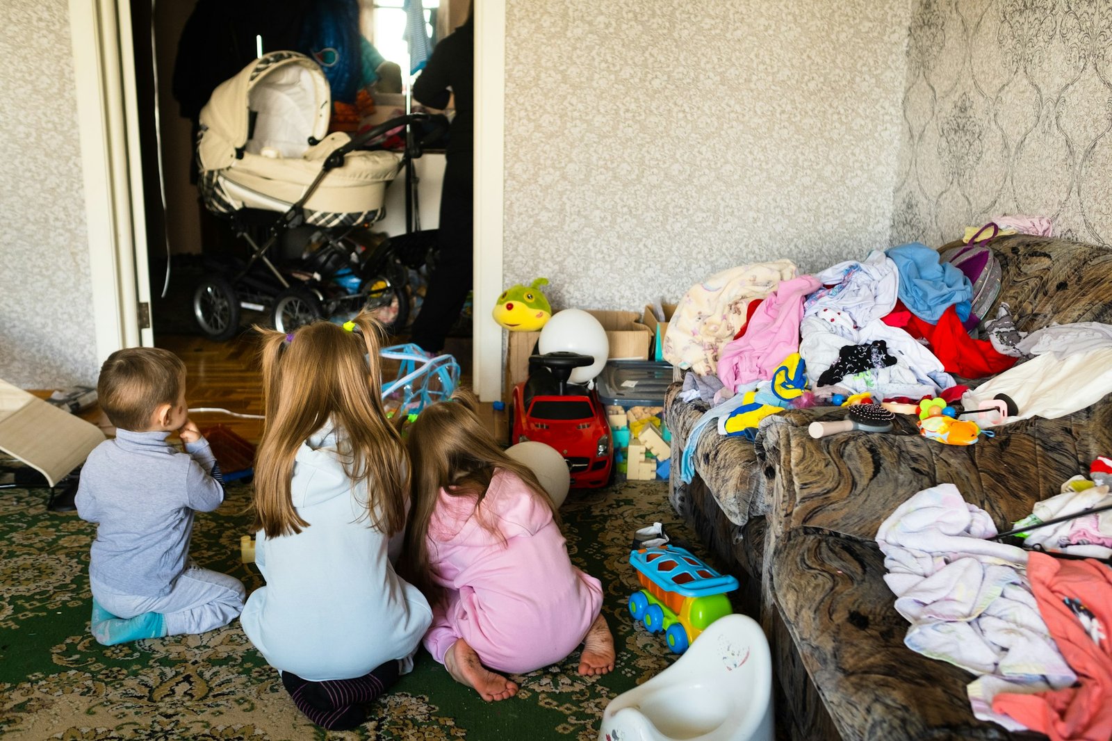 Three unrecognizable children are playing in a dirty cluttered room