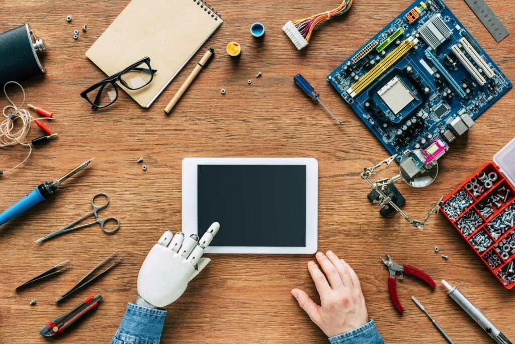 cropped image of man with robotic hand using digital tablet at table surrounded by tools