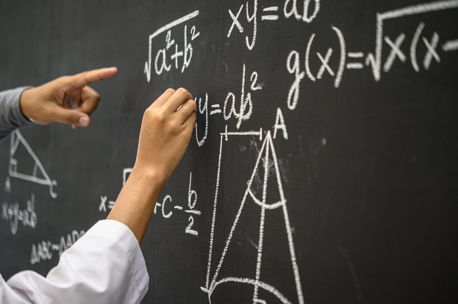 Hands pointing to mathematical equations on a chalkboard