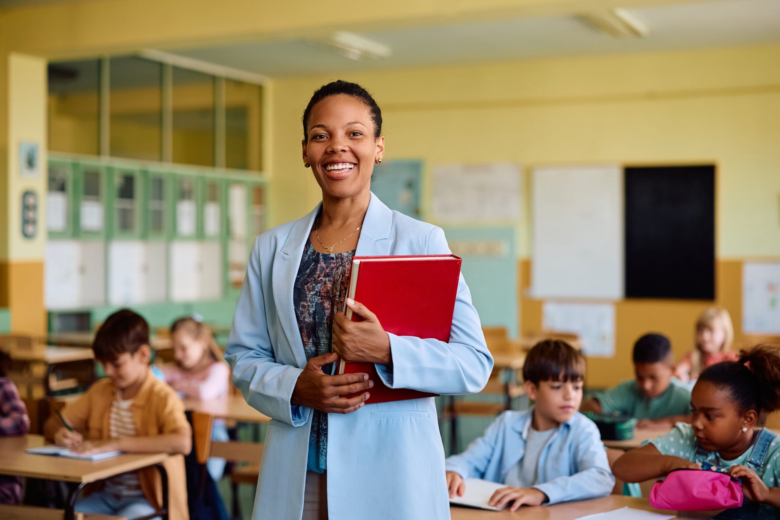 A smiling teacher holding a folder in a classroom